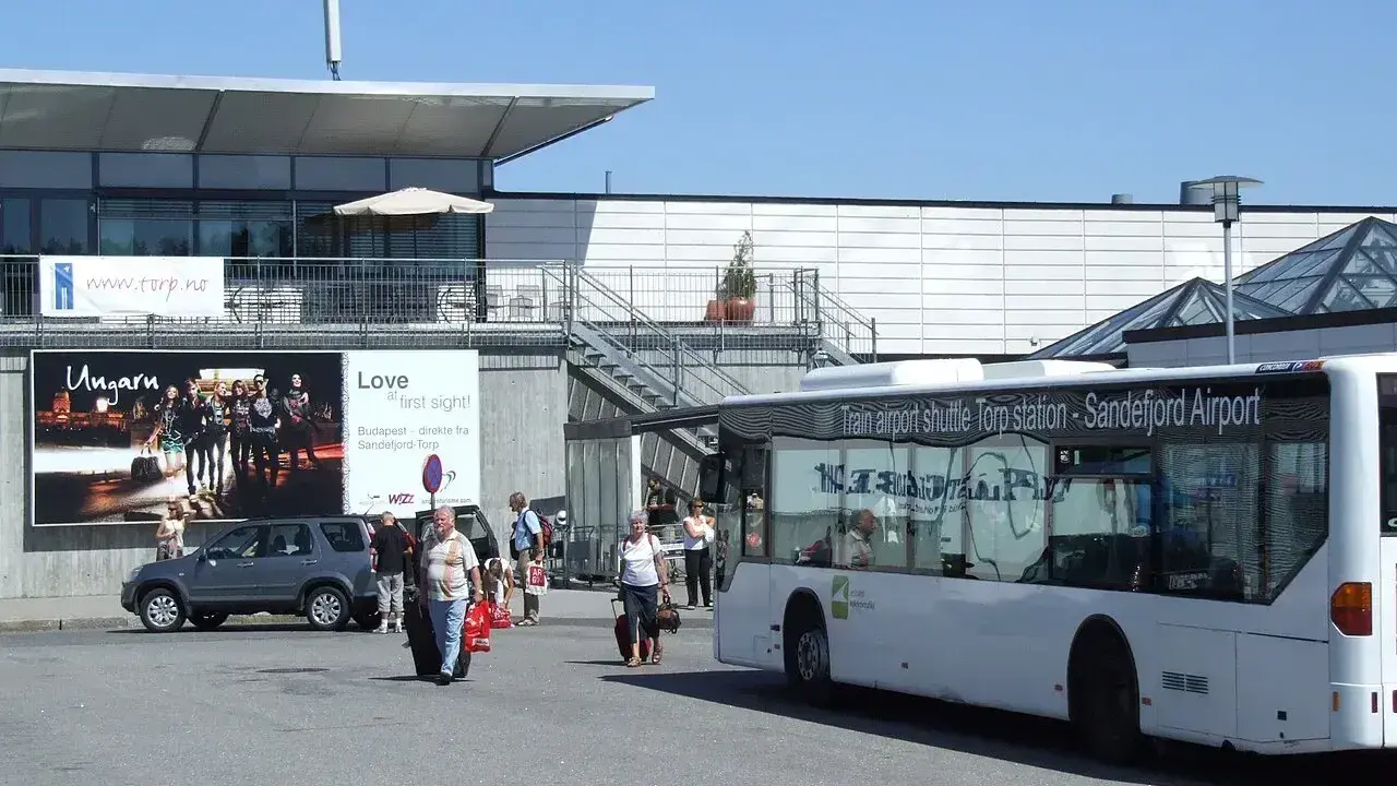 Autobus wahadłowy na lotnisko Oslo Torp. Ludzie z bagażami wychodzą z terminala.