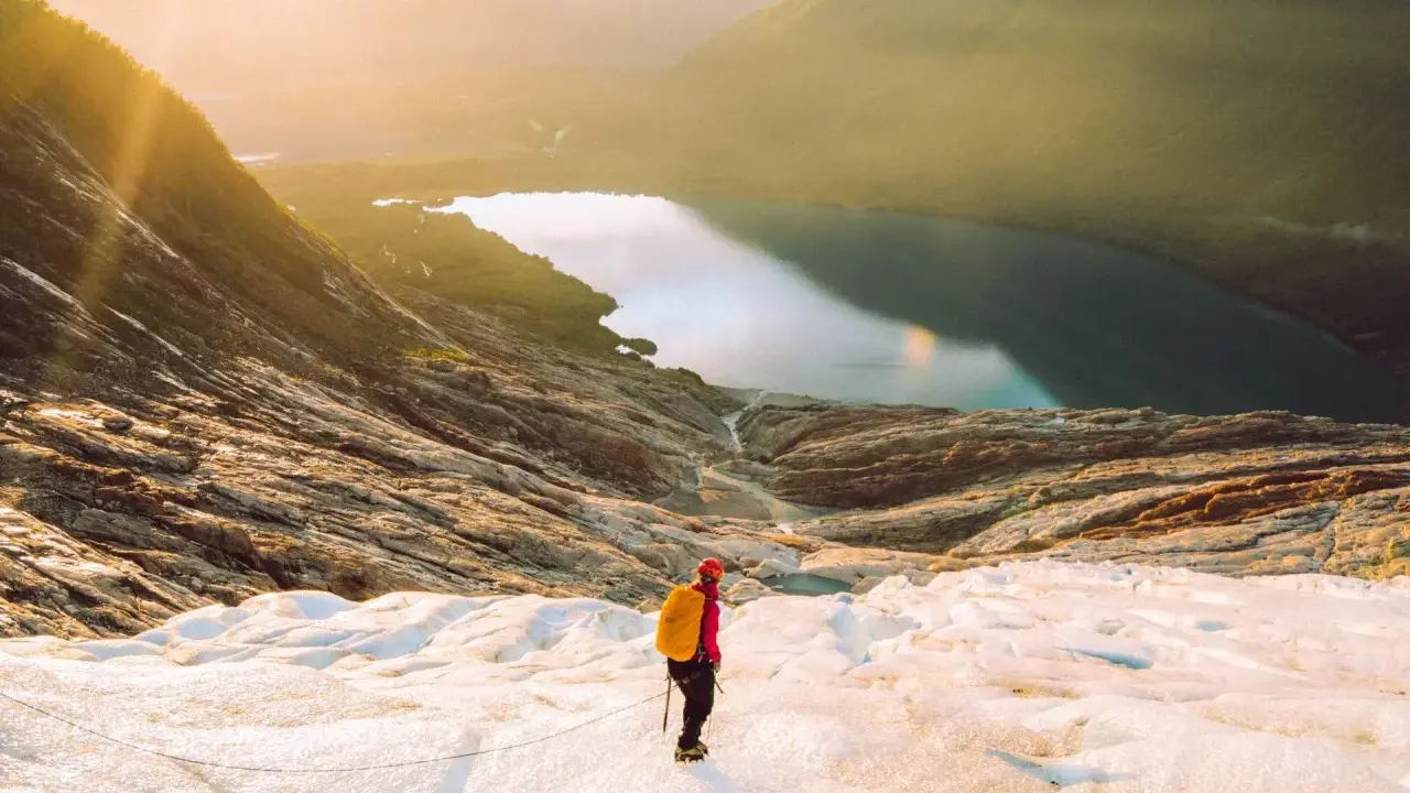 Vandrare på en glaciär i Norge med en sjö och berg i bakgrunden. En av många norge sevärdheter.