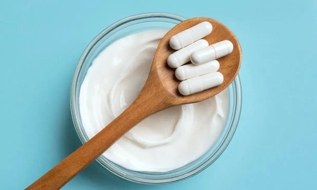 Cuillère en bois avec des gélules blanches sur un yaourt crémeux. Une question se pose : quel probiotique pour maigrir ?