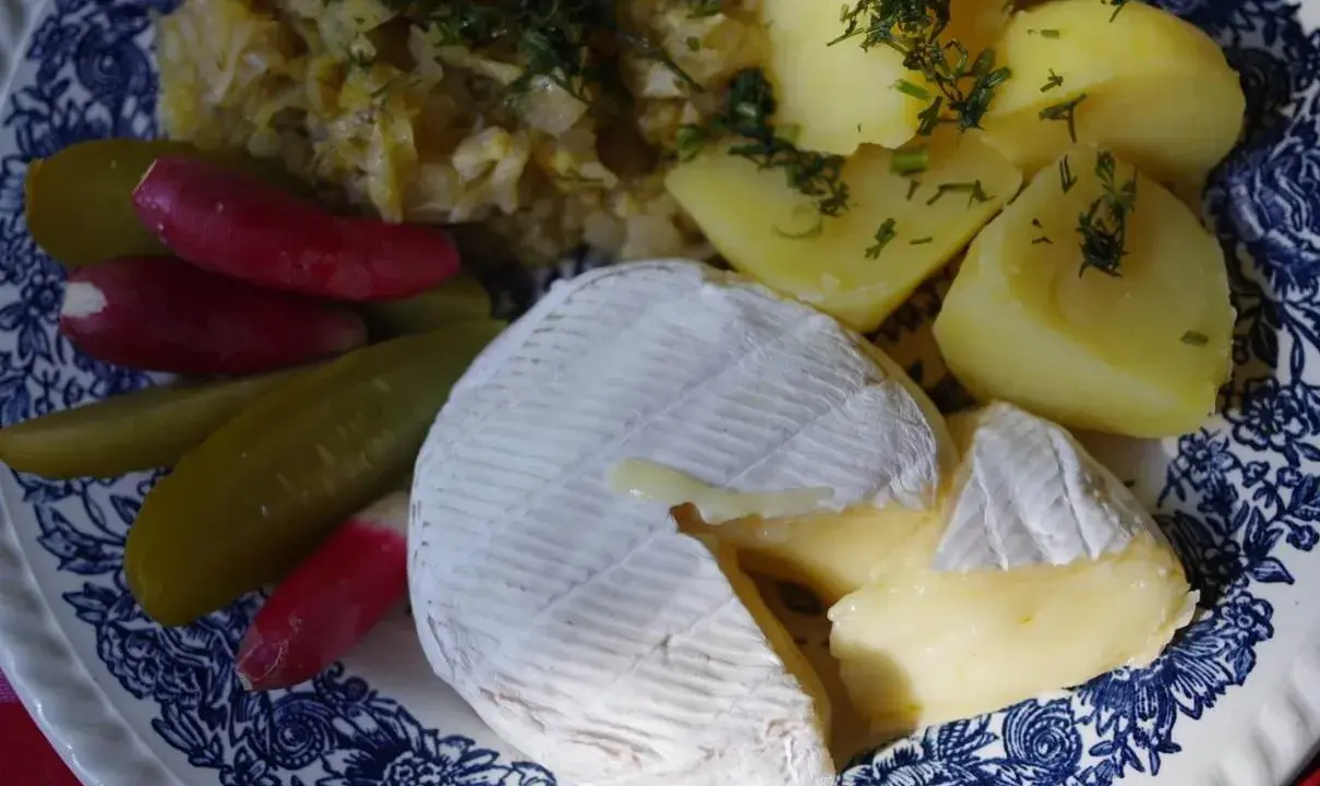 Częściowo roztopiony camembert z ziemniakami, ogórkami kiszonymi i rzodkiewką na talerzu.