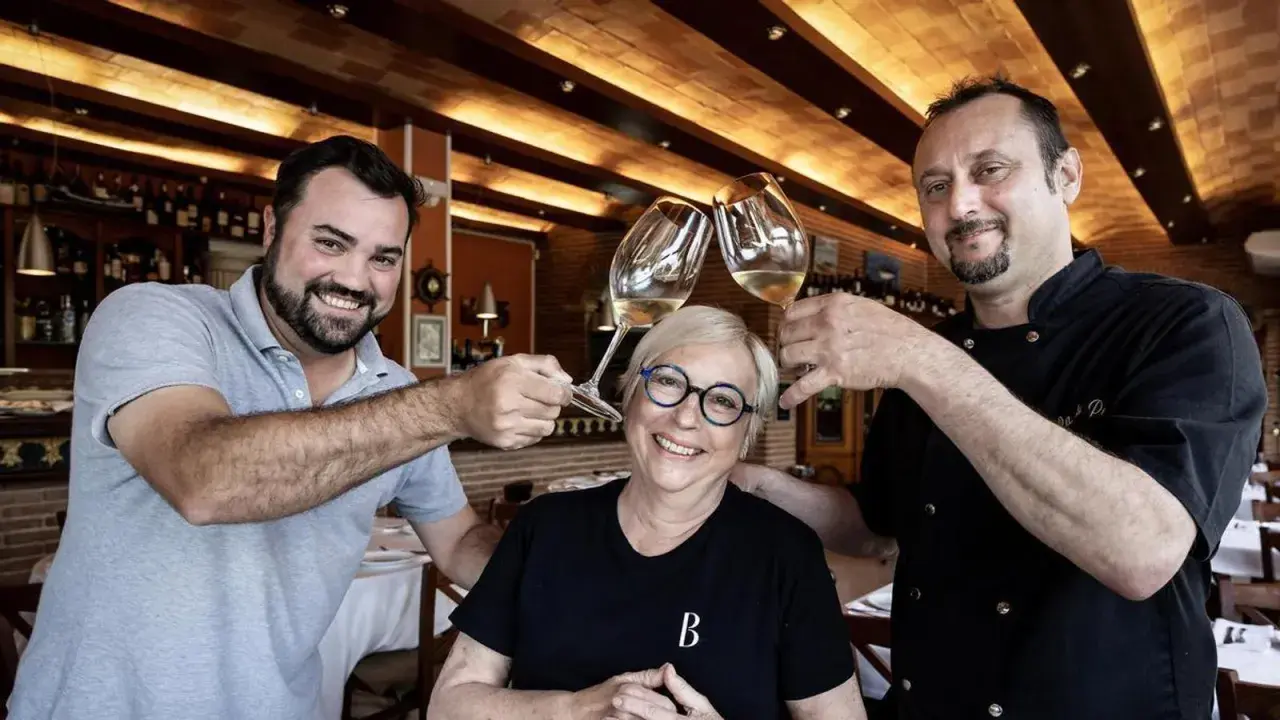 Dos hombres y una mujer brindan con copas de vino en Ca la Pepa, un restaurante acogedor con estanterías de vino.