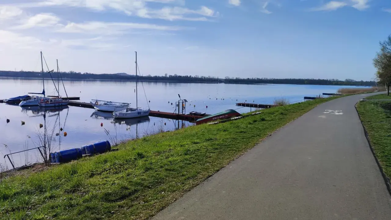 Jezioro Pogoria 4 z łodziami przy pomoście i ścieżką rowerową.
