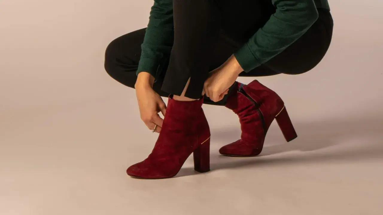 Eine Frau zieht rote Wildleder-Stiefeletten an. Verschiedene lederarten schuhe sind hier zu sehen, wie diese eleganten Damenschuhe.