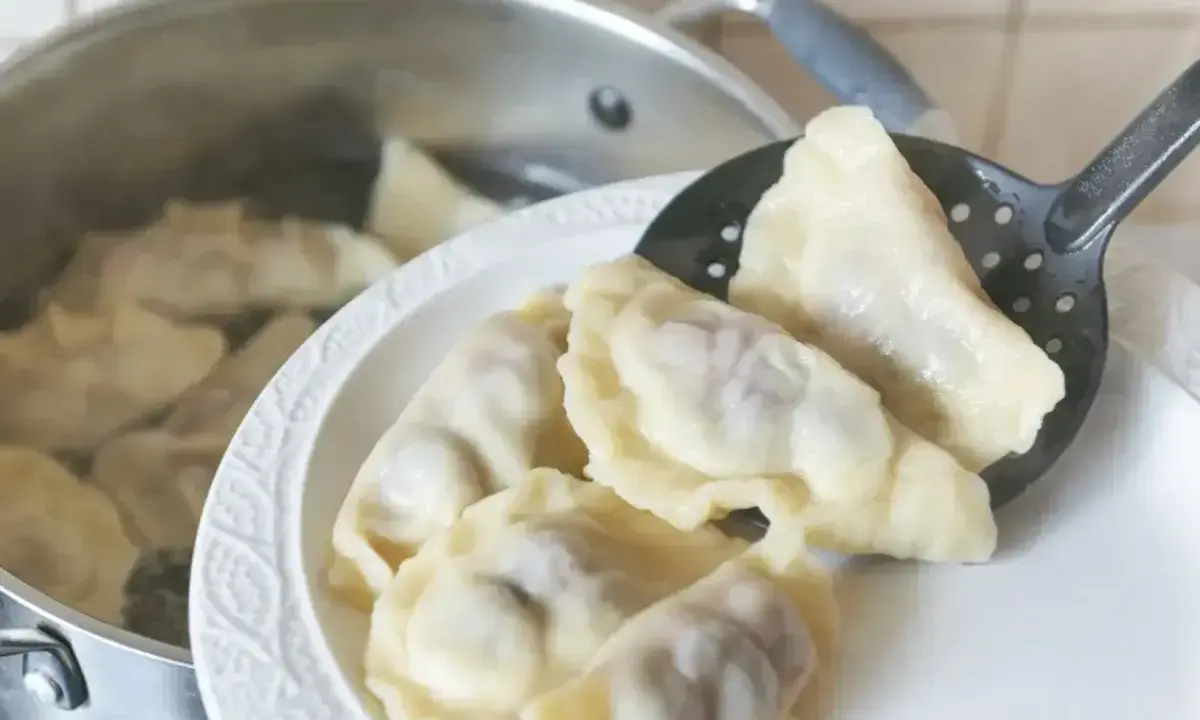 Gotowanie pierogów: gdy wypłyną na powierzchnię, gotuj jeszcze 2-3 minuty. Na talerzu czeka porcja świeżo ugotowanych, parujących pierogów.