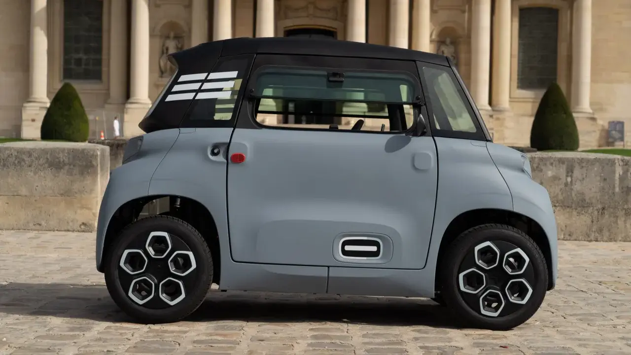 Une petite voiture grise, un ami pour la ville, se gare devant un bâtiment imposant.