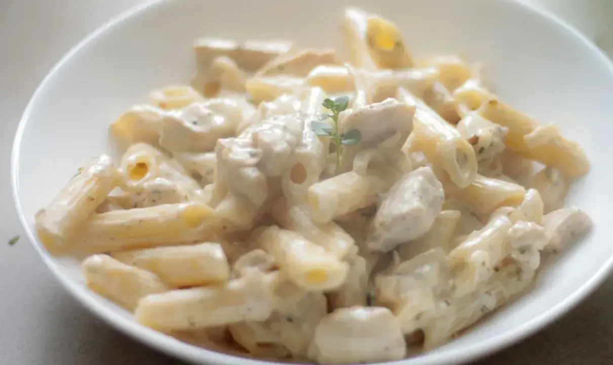 Penne z kremowym sosem i kawałkami kurczaka, udekorowane gałązką ziół. Pyszna potrawka z kurczaka w sam raz na obiad.