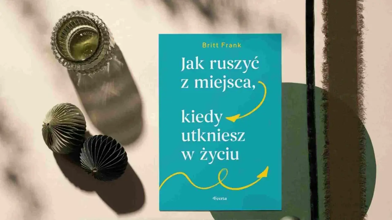 Książka "Jak ruszyć z miejsca, kiedy utkniesz w życiu" Britt Frank. Obok szklanka z napojem i ozdobne kule. Idealna lektura, gdy dopada lenistwo.
