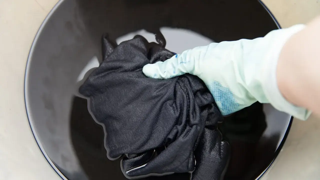 Mano con guante sumerge ropa blanca desteñida de negro en tinte oscuro.