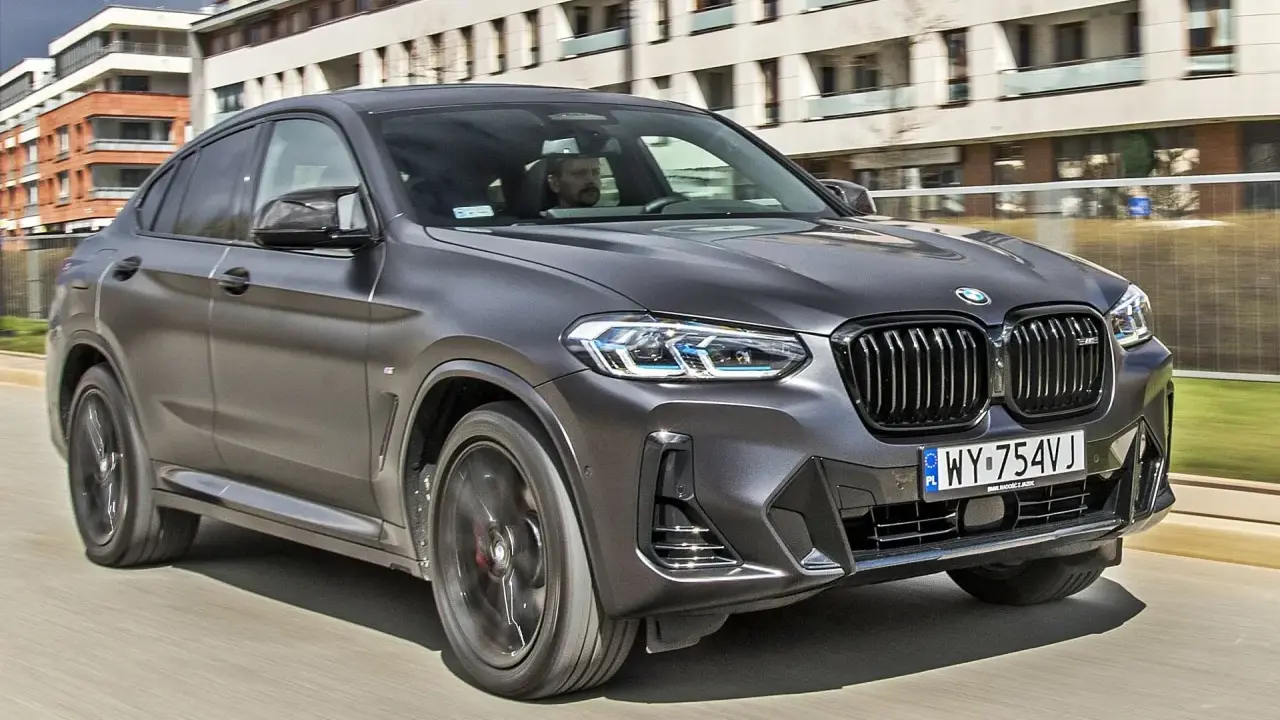Nowy BMW X4 2025 w ciemnoszarym kolorze pędzi ulicą, z nowoczesnymi budynkami w tle.