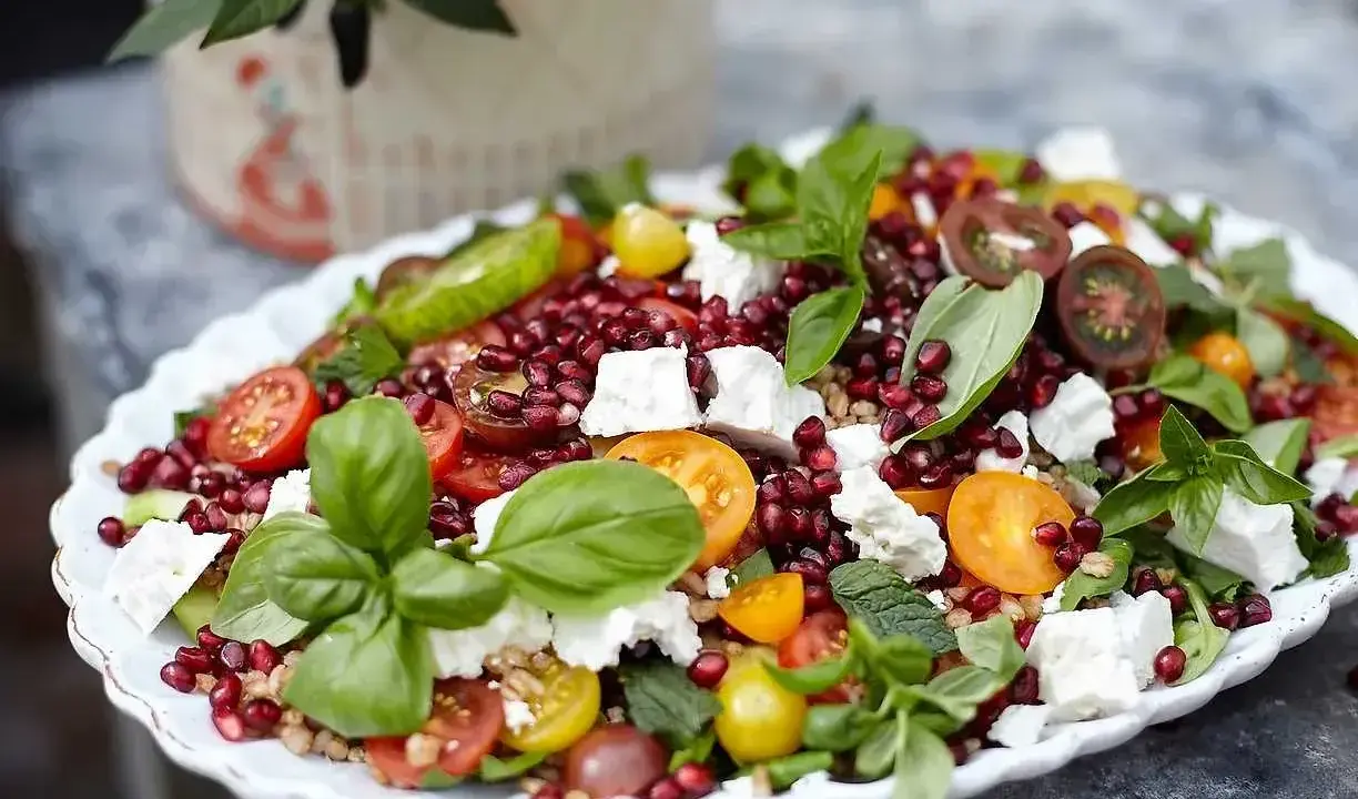 En färgglad sallad med granatäpple, tomater, fetaost och basilika, perfekt som sallad till grillat.
