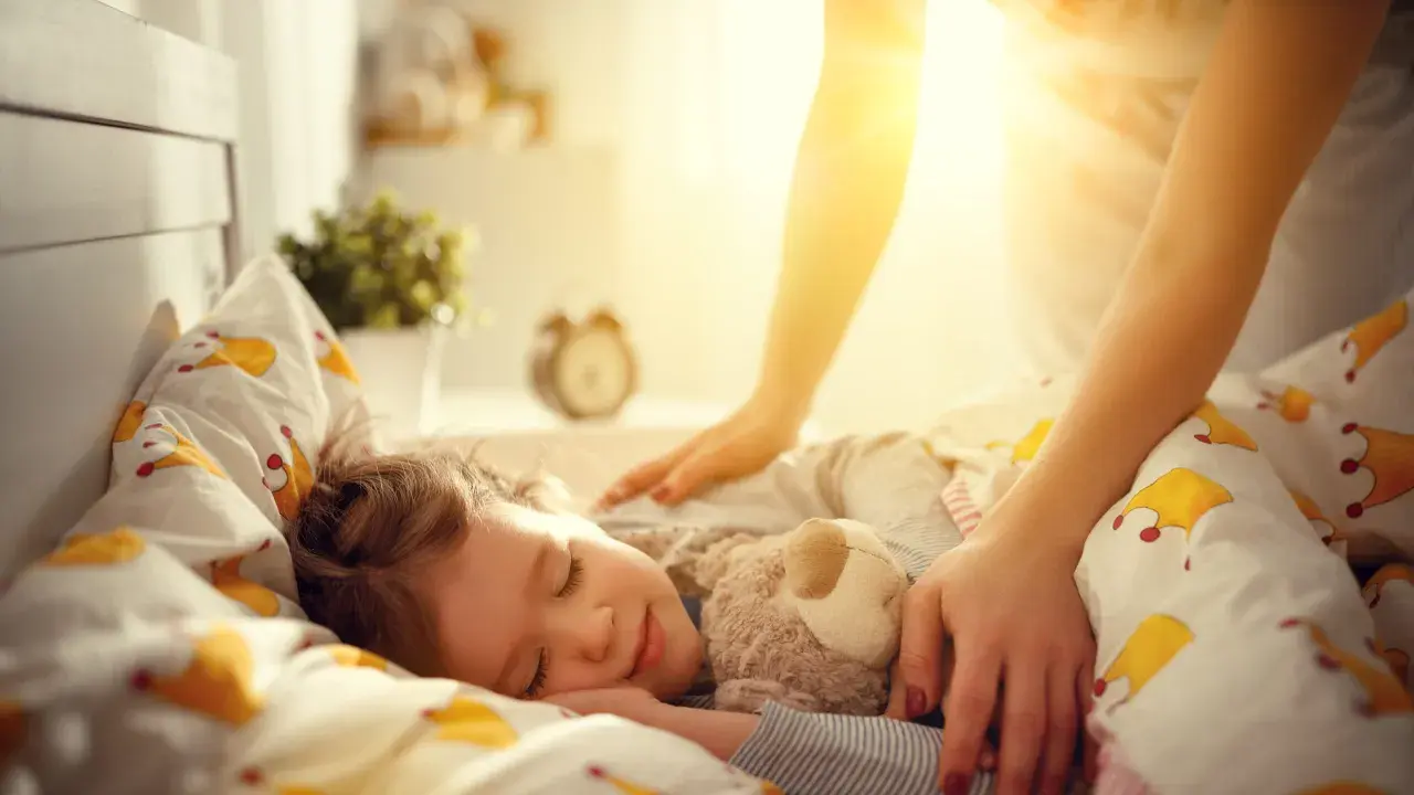 Mama pomaga dziecku zasnąć, kładąc rękę na jego ramieniu. Słodki sen malucha to pierwszy krok, jak nauczyć dziecko zasypiać samo.
