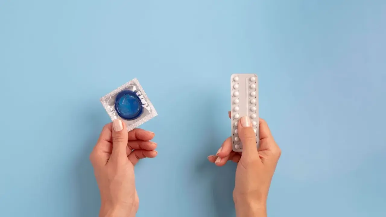 Manos sostienen un preservativo y pastillas anticonceptivas, mostrando opciones de planificación familiar.