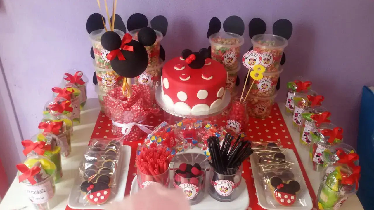 Mesa de fiesta temática de Minnie Mouse con pastel, galletas, palomitas y muchos centros de chuches para niños.