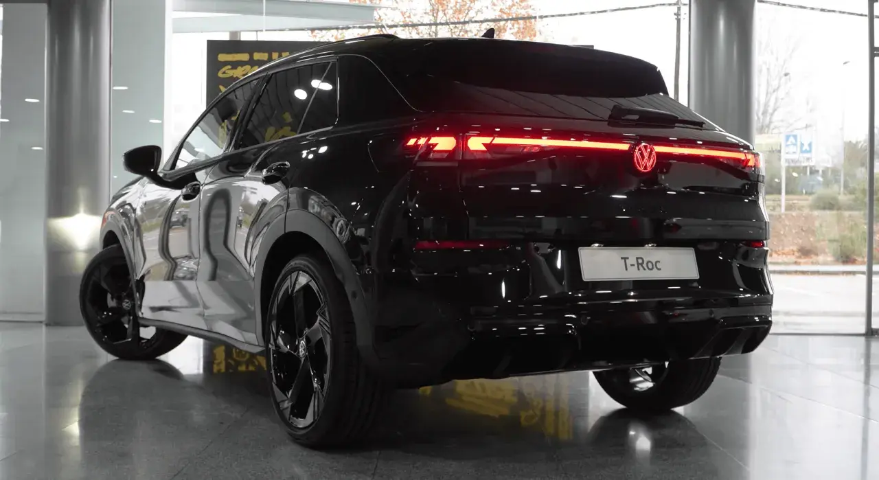 El Volkswagen T-Roc 2026 negro brillante, con sus luces traseras LED rojas encendidas, se exhibe en un concesionario.