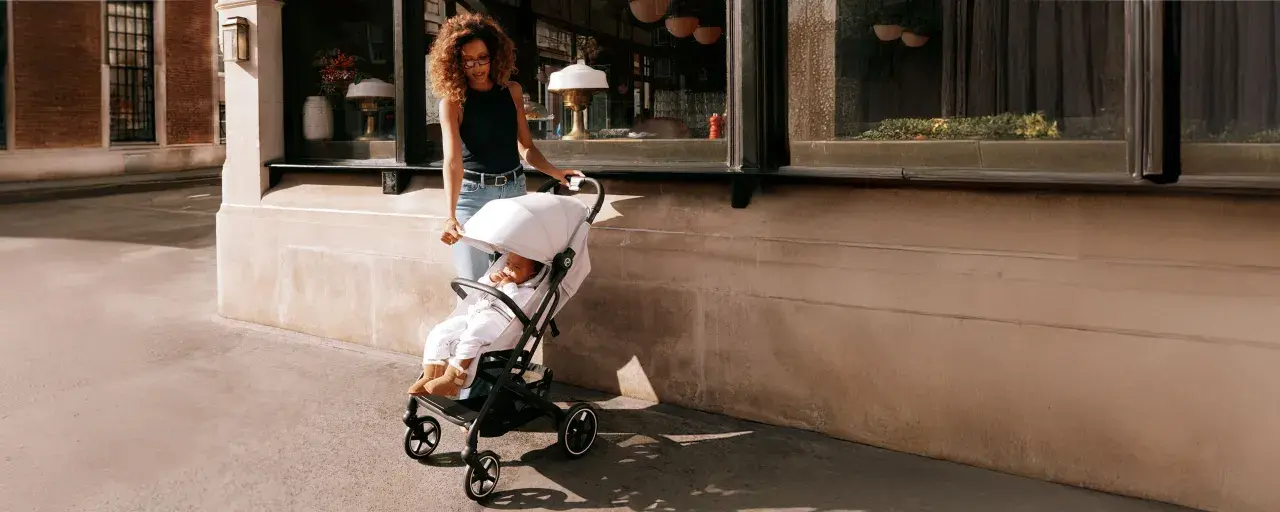 Kobieta prowadzi dziecko w wózku Cybex Beezy ulicą.