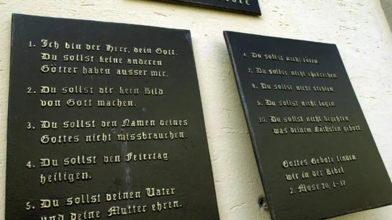 Die **10 Gebote katholisch** auf schwarzen Tafeln an einer Wand. Sie lehren uns, Gott zu ehren und den Nächsten zu lieben.