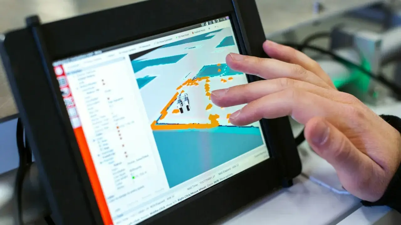 Ein Finger tippt auf ein Tablet, das eine 3D-Ansicht mit einem Roboter zeigt. Die dji app windows wird zur Steuerung genutzt.