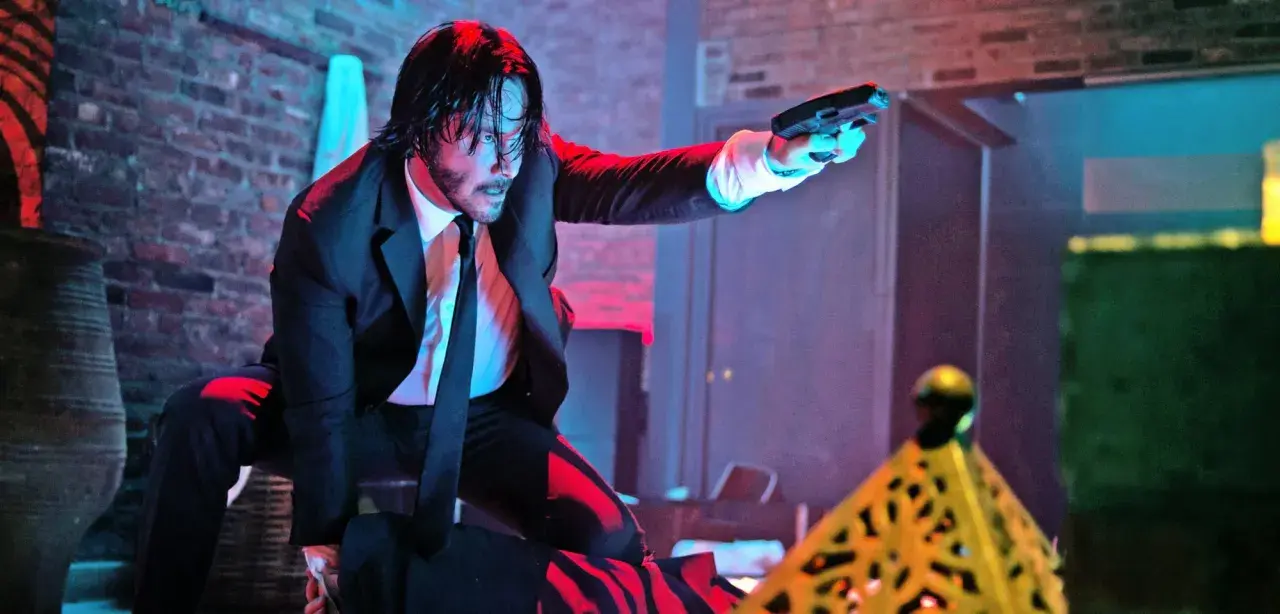 John Wick i svart kostym, med pistol i hand, redo för strid. Kanske en scen från John Wick 5.