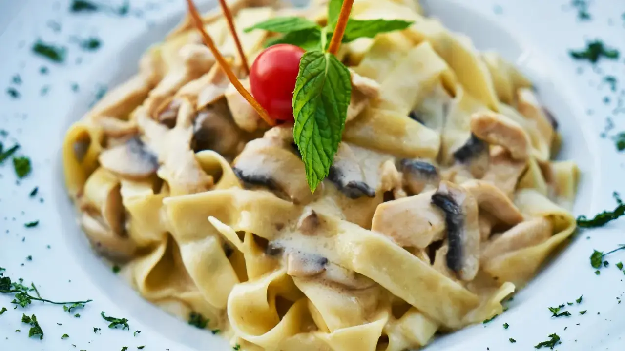 Tagliatelle z kurczakiem w sosie śmietanowym, z pieczarkami i pomidorkiem koktajlowym, udekorowane listkiem mięty.