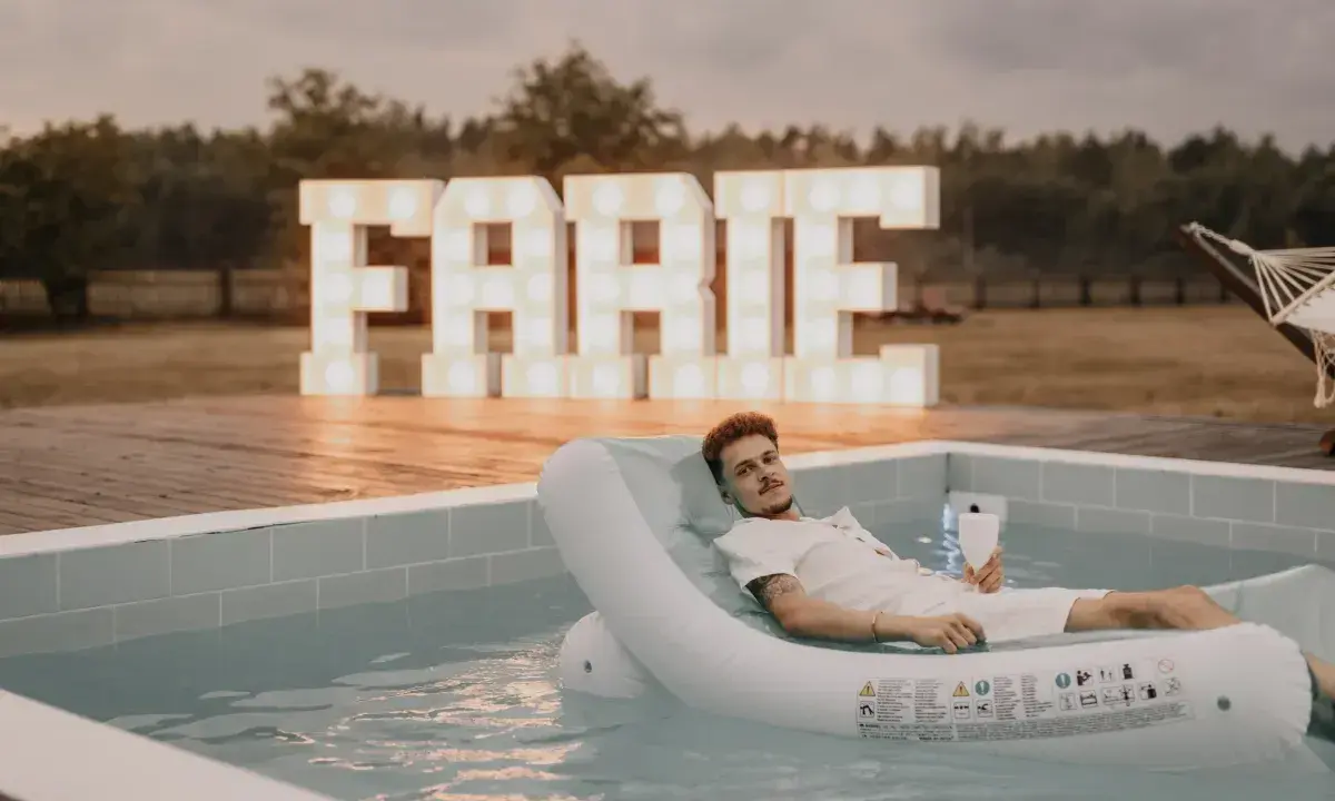 Relaks przy basenie z drinkiem, wielkie litery "FARTE" w tle. Idealny pomysł, jak zorganizować wieczór kawalerski.