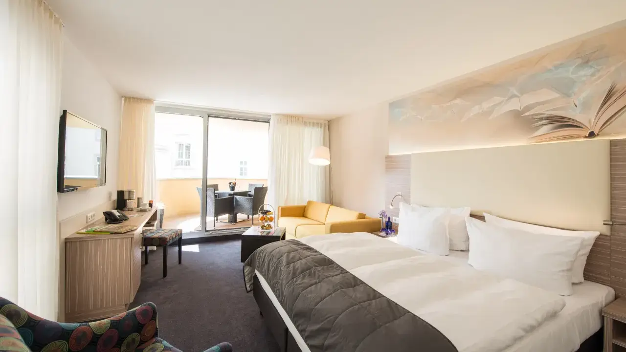 Modernes Hotelzimmer mit Doppelbett, Sofa, Schreibtisch und Balkon.