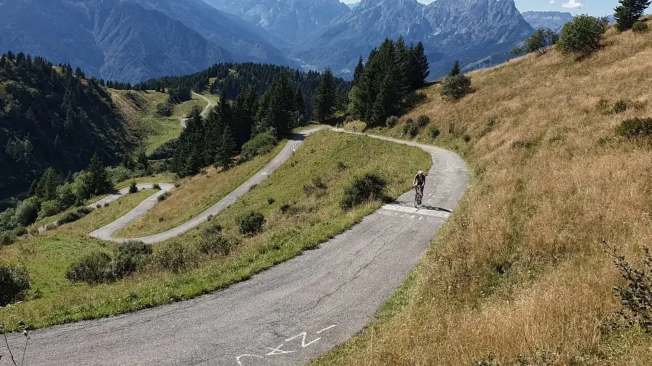 Radfahrer kämpft sich die Serpentinen des Monte Zoncolan hoch. Majestätische Berge im Hintergrund.