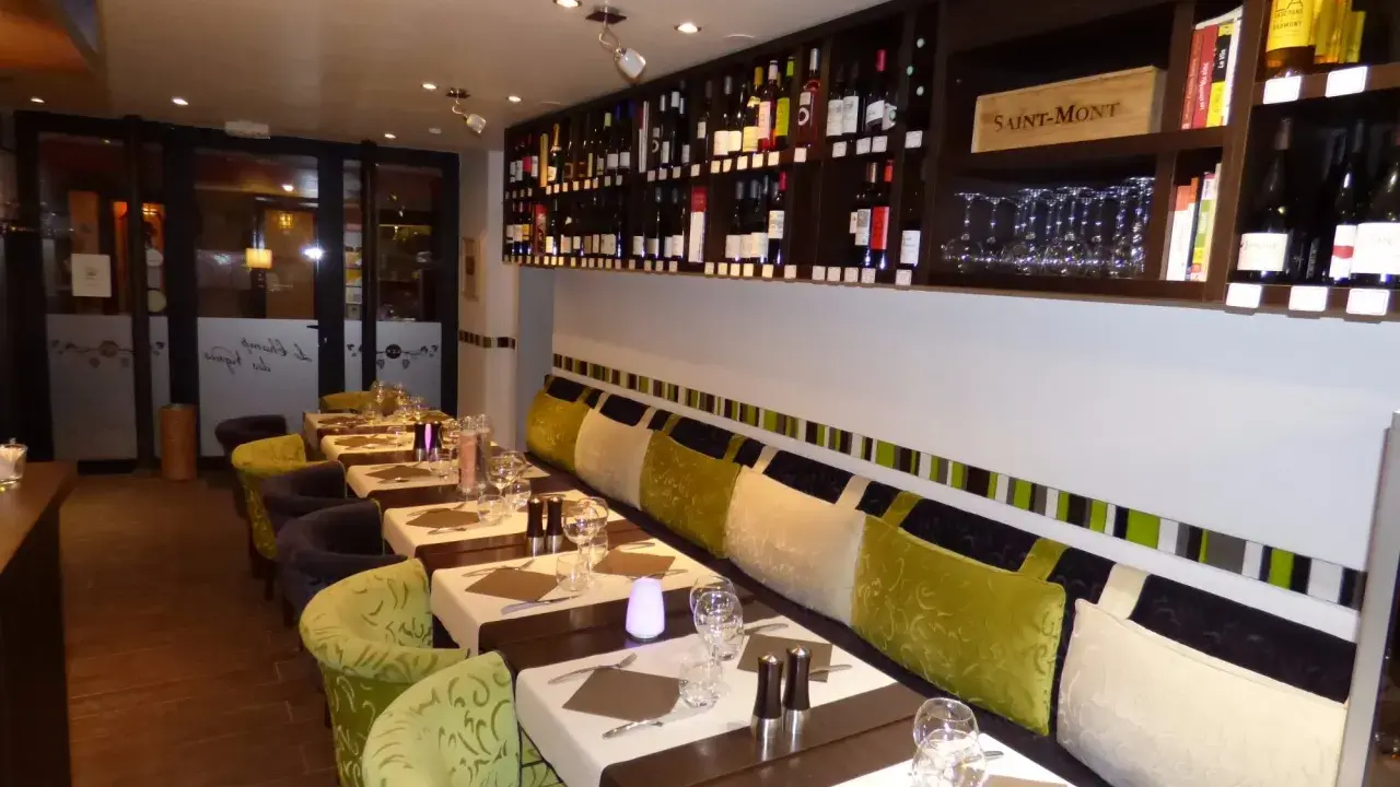 Tables dressées dans un restaurant à Aurillac, idéal pour un repas du dimanche. Les étagères débordent de bouteilles de vin.