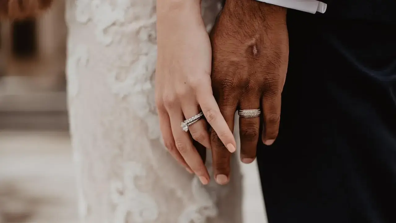 Manos entrelazadas, mostrando el anillo de casada en la mano izquierda de ella y el de él en la derecha.