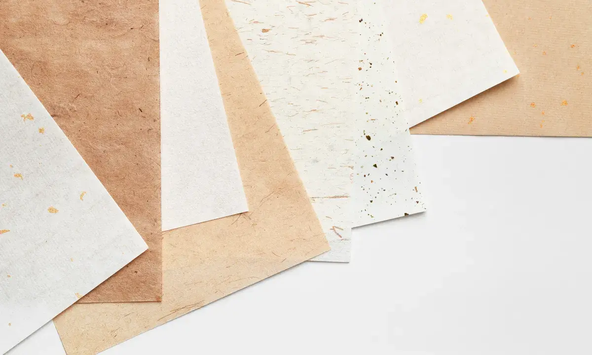 Różne rodzaje papieru, od jasnych po brązowe, z delikatnymi zdobieniami. Każdy papier to inna klasa papieru, idealna do twórczych projektów.