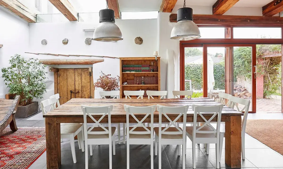 Tavolo rustico con sedie bianche, ideale per un agriturismo ristorante Trento e dintorni. Luce naturale da grandi vetrate.