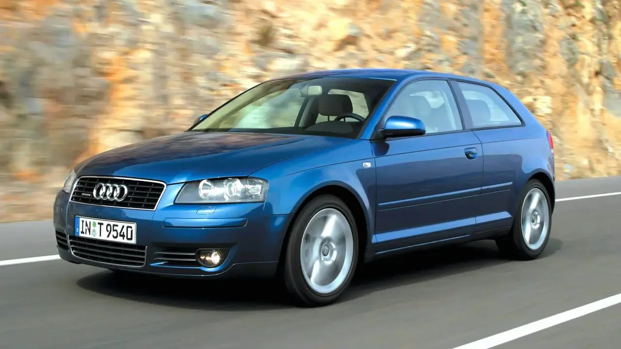 Niebieskie Audi A3 8P w ruchu, z widocznymi przednimi żarówkami, pędzi po drodze wśród skalistych zboczy.