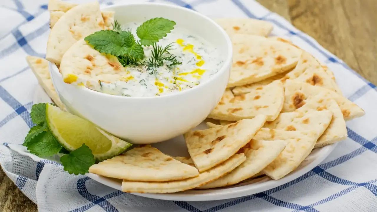 Un bol de tzatziki crémeux garni d'herbes fraîches, servi avec des morceaux de pain pita croustillants. Parfait pour tremper !