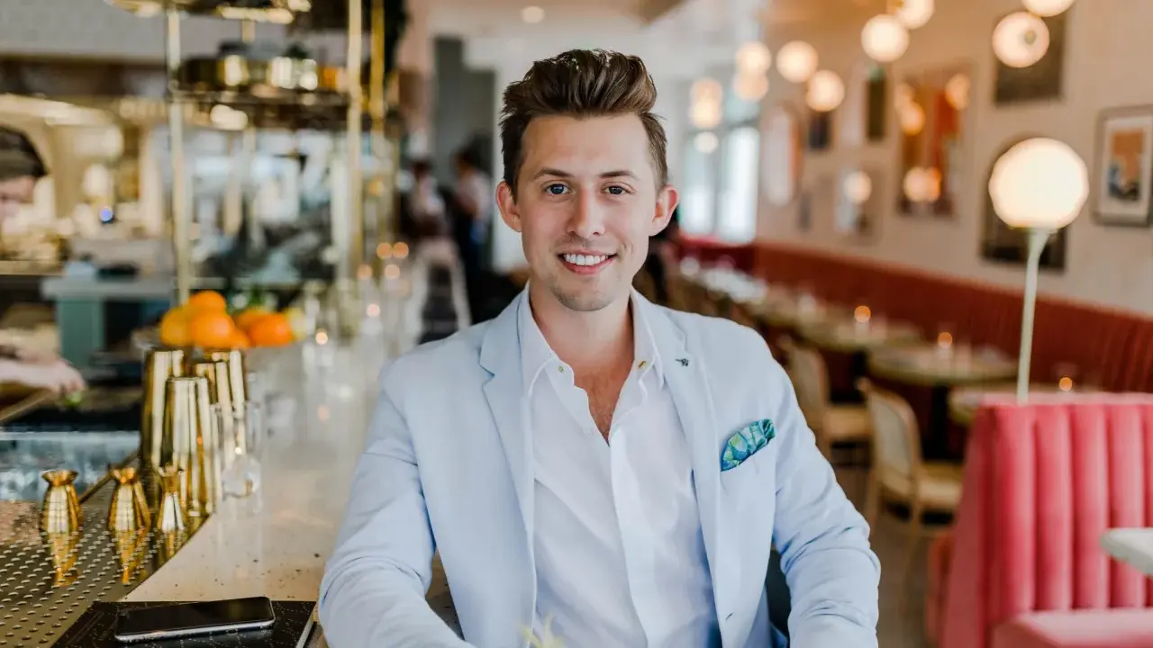 Uśmiechnięty menedżer firmy w jasnoniebieskiej marynarce siedzi przy barze w eleganckiej restauracji.