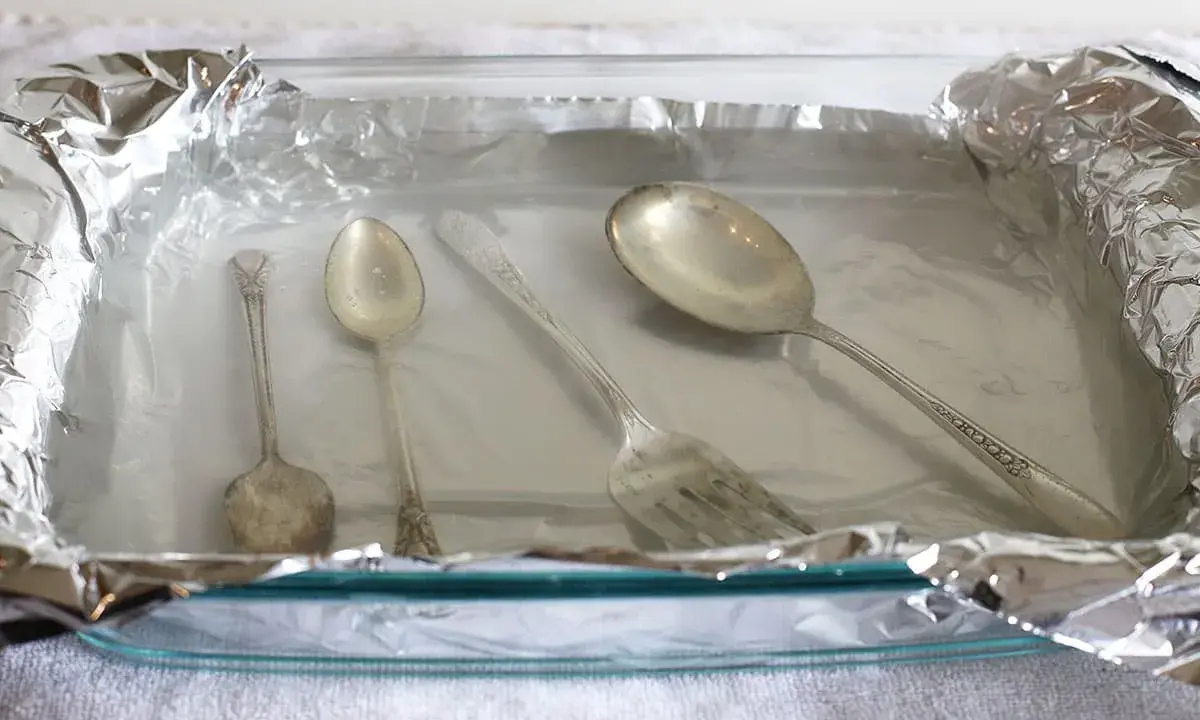 Srebrne sztućce w szklanej misce wyłożonej folią aluminiową.