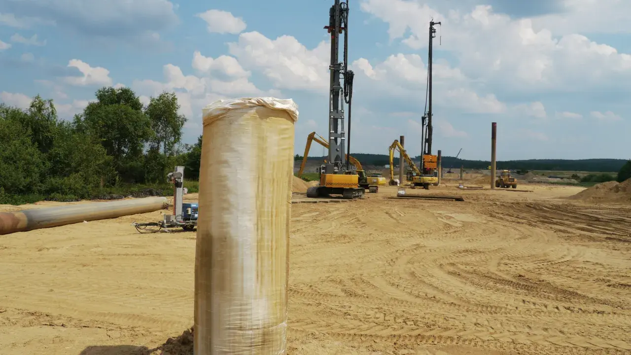 Construcción en terreno arenoso, con maquinaria pesada y tuberías. Se aprecian varios tipos de suelos blandos, listos para la obra.