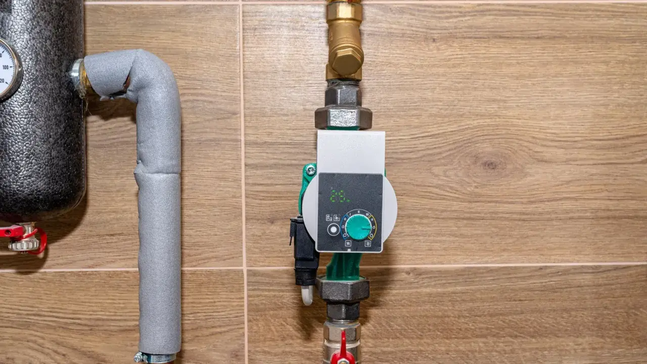 Nowoczesna pompa cyrkulacyjna a obiegowa z cyfrowym wyświetlaczem i pokrętłem regulacji, zamontowana na rurach instalacji grzewczej.