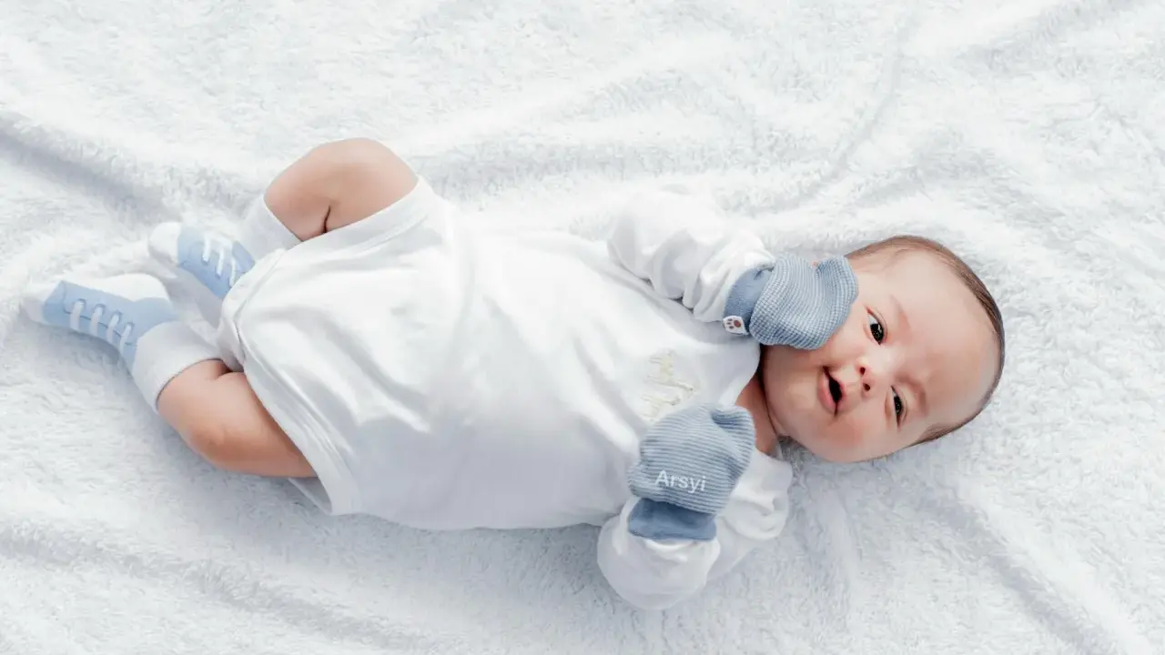 Dolce neonato nel suo primo mese, sdraiato su un soffice telo bianco, con calzini azzurri e guantini.