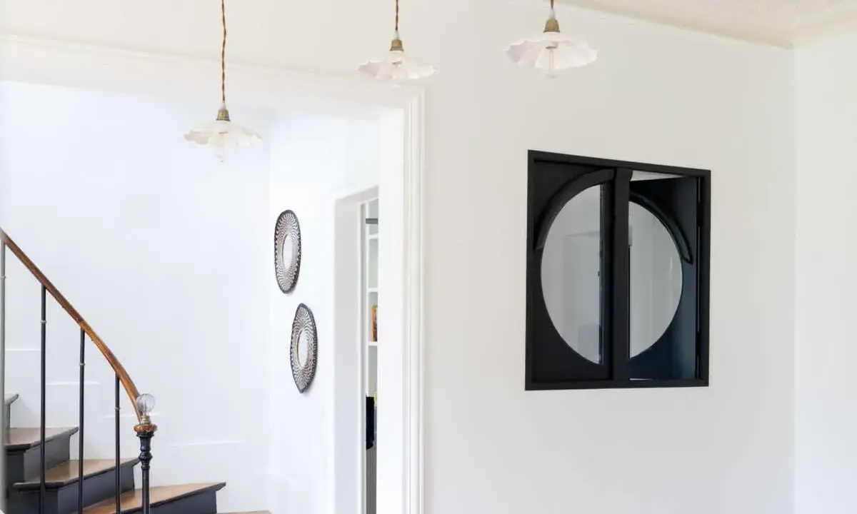 Entrée lumineuse avec escalier aux marches en bois et contremarches noires. Quelle couleur pour une entrée avec escalier ? Ici, le blanc éclatant met en valeur le design.