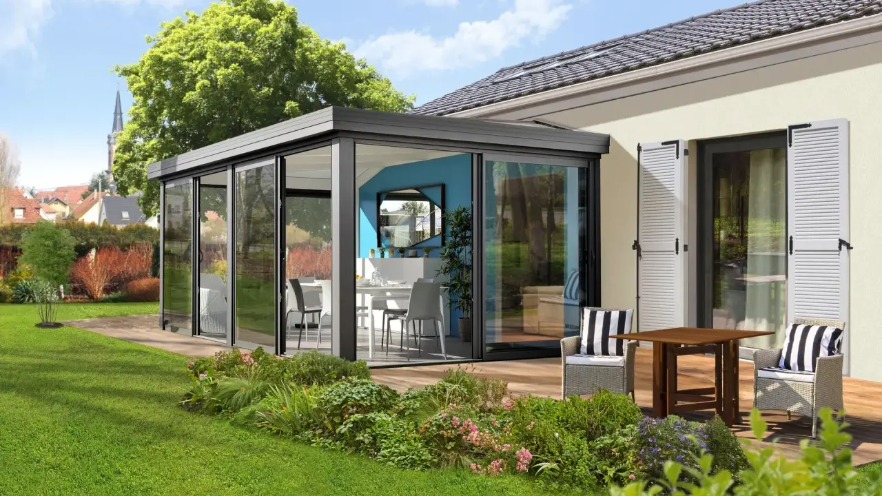 Moderne veranda sans permis de construire, avec table et chaises, offrant une vue sur un jardin verdoyant et des maisons.