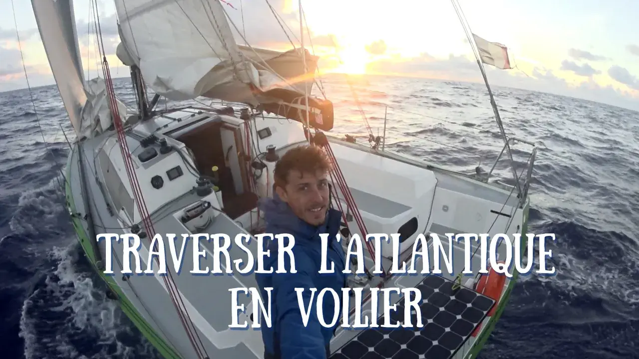 Un homme souriant sur un voilier navigue sur l'océan au coucher du soleil. Quel bateau pour traverser l'Atlantique ? Ce voilier semble prêt pour l'aventure.