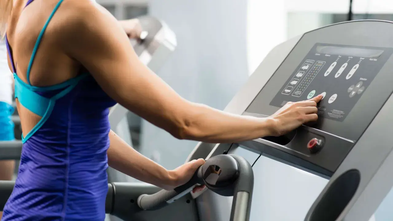 Frau stellt Steigung für ihr **incline walking** auf dem Laufband ein.