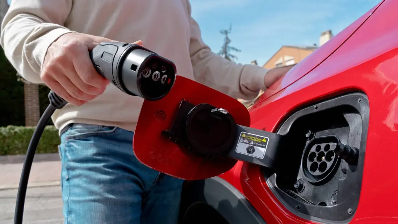 Persona desconectando el cargador de un coche eléctrico rojo.