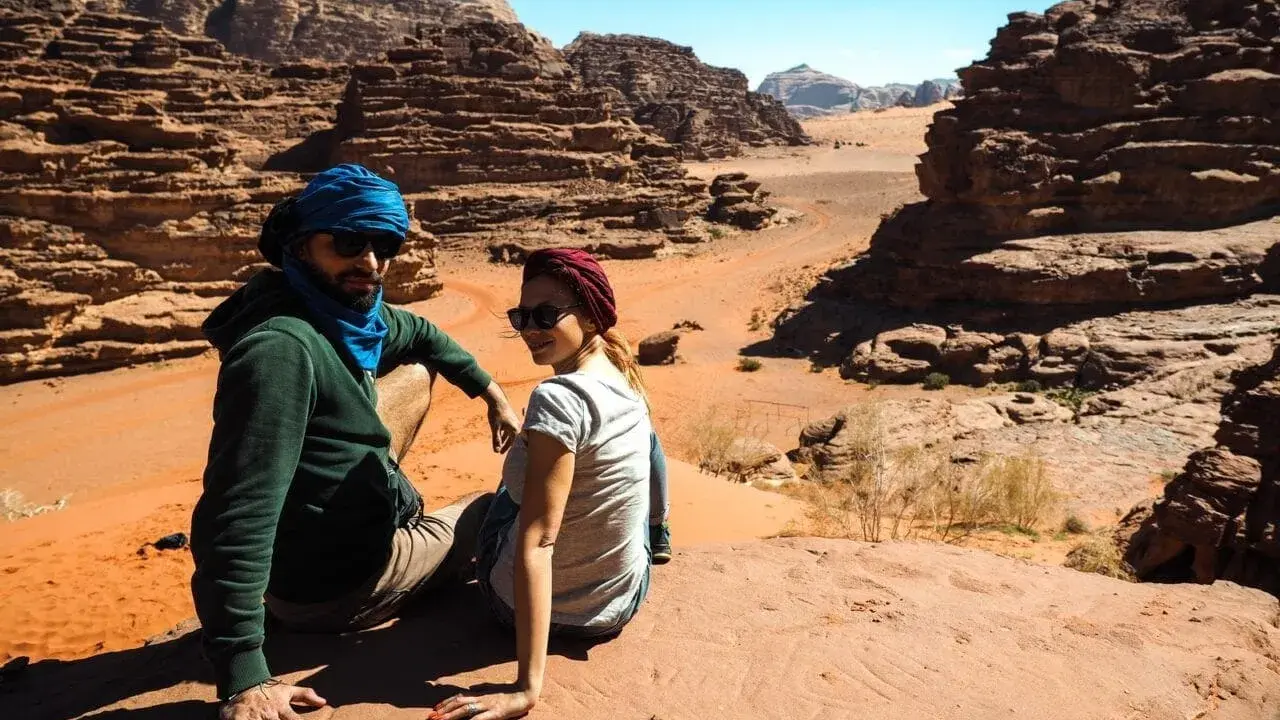 Para w turbanach odpoczywa na piasku, podziwiając skaliste krajobrazy pustyni Wadi Rum.