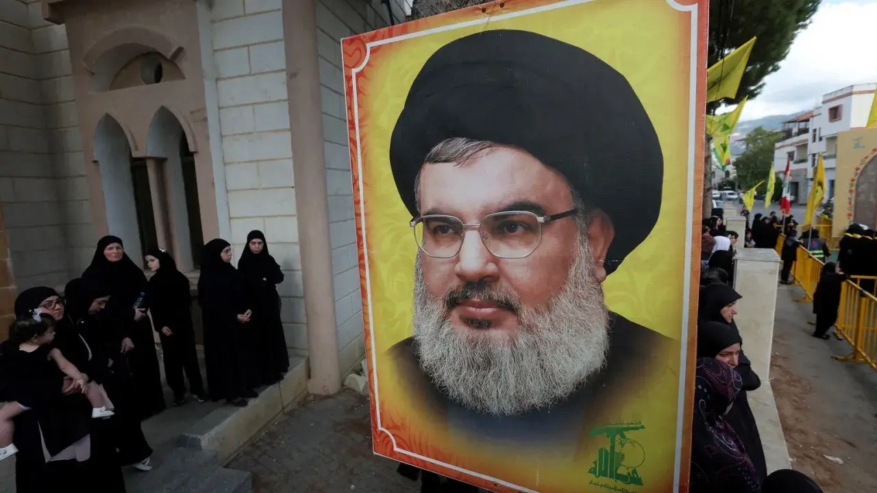 Wielki portret Hassana Nasrallaha, lidera Hezbollah, obok grupy kobiet w czarnych hidżabach.
