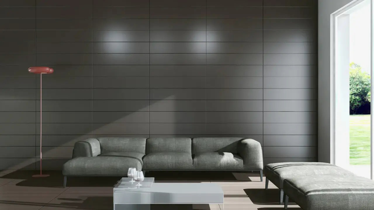Nowoczesny salon z szarą kanapą i pufą. Zastanawiasz się, jakie płytki do salonu? Spójrz na te ciemne, eleganckie płytki na ścianie i jasne na podłodze.