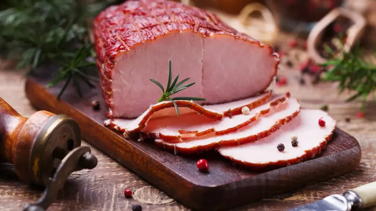Pokrojona szynka wieprzowa z rozmarynem i pieprzem na desce.