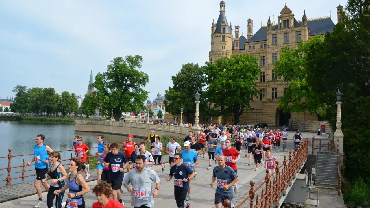 Teilnehmer des 5 Seen Lauf Schwerin überqueren eine Brücke vor dem Schloss.