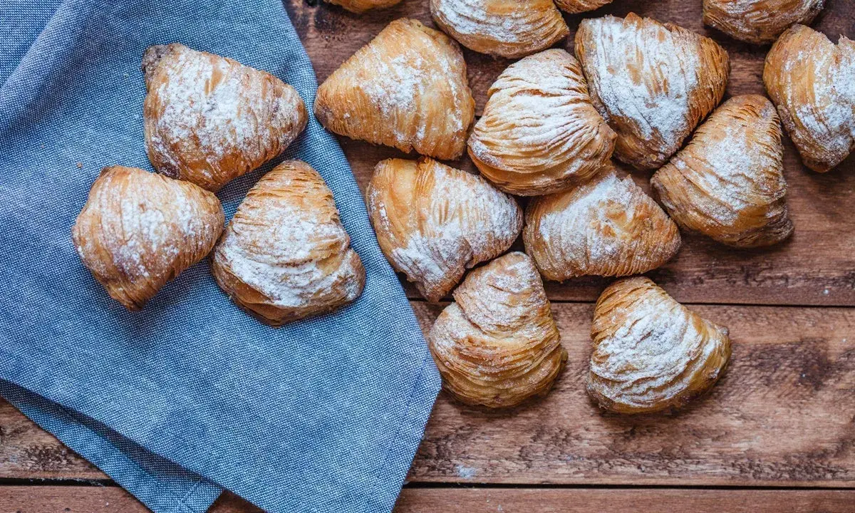 Sfogliatelle, un delizioso cibo tipico napoletano, cosparse di zucchero a velo su un tavolo di legno e un tovagliolo blu.