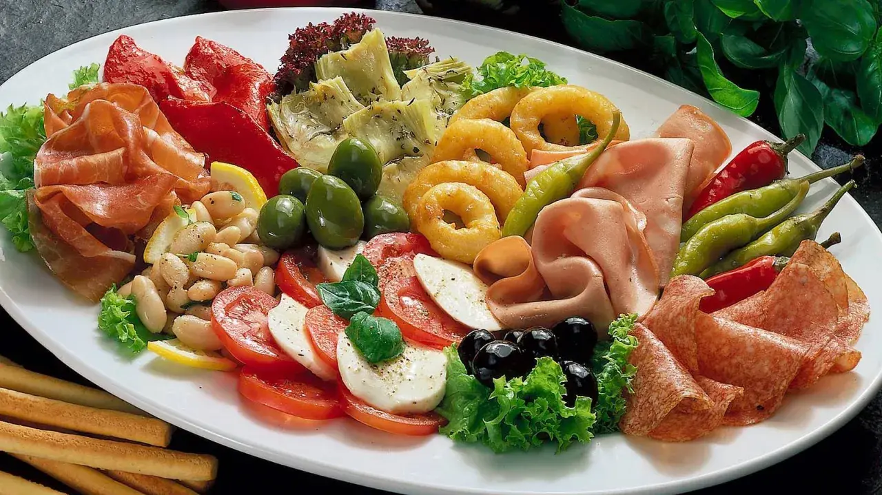 Eine üppige Platte mit italienischen Vorspeisen: Prosciutto, Salami, Mozzarella, Tomaten, Oliven, Artischocken, Bohnen und eingelegte Paprika.