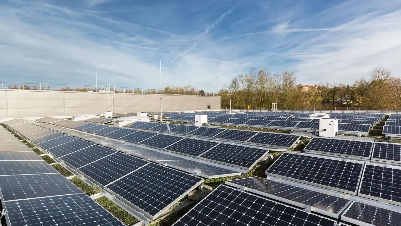 Stora fält av solpaneler på ett tak, med flera vita, små växelriktare utplacerade bland dem.